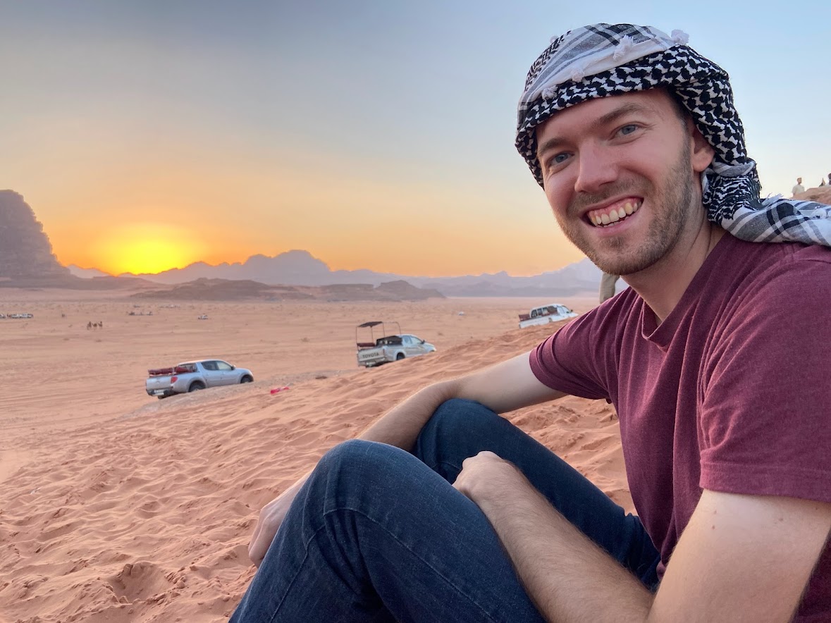 A man sitting on a sand dune overlooking a sunset